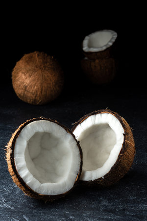 Coconut on a black background. Chopped coconut. Several parts. Stone surface. Fresh coconut. White...
