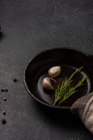 Empty black cast iron frying pan on a dark graphite background. Light linen towel. Fresh rosemary.の写真素材