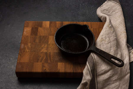 Empty black cast iron frying pan on a dark graphite background. Light linen towel. Wooden end cutting board. Fresh rosemary.の写真素材