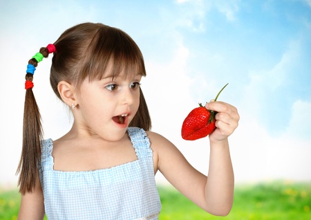 Funny surprised child girl with strawberry, field on background の写真素材