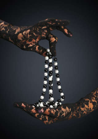 gloved hands hold jewelry necklace on dark backgroundの写真素材