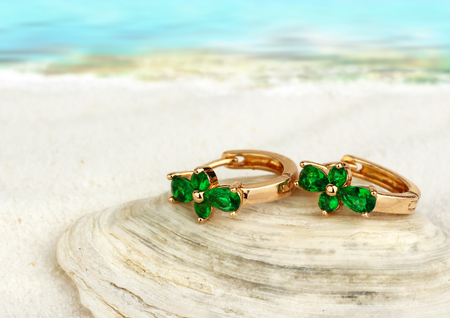 Jewellry earrings with emerald on sand beach with, soft focusの写真素材