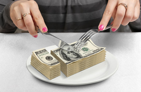 Hands cut money on plate, reduce funds conceptの写真素材