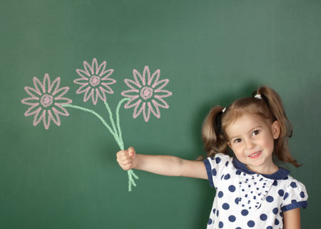 Smiling child hold drawn flowers near school blackboardの写真素材
