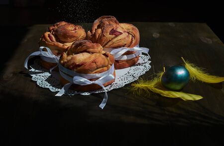 side view of kraffins with white ribbons on a lace napkin with yellow feathers and an easter egg on a wooden backgroundの写真素材