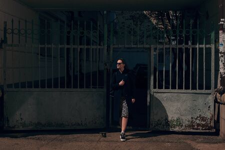 masked girl against coronavirus walking the streets of the city on a sunny day in a coat and fashionable glassesの写真素材