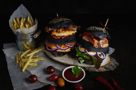 black double burgers on a wooden board and dark background with fries tomatoesの写真素材