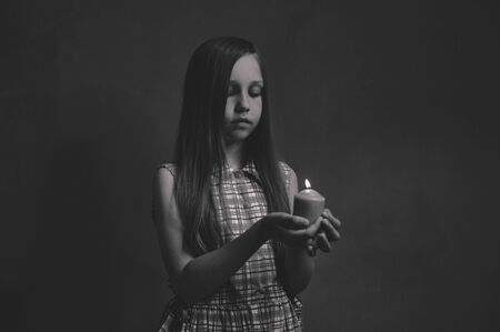 The girl stands with a candle on a dark background. black white photoの写真素材