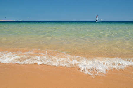 Wave on a sandy beach, blue clear water on the horizon the sails of Windsurfing.の写真素材