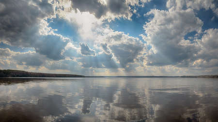 Rays of sun shining through the clouds. The river runs into the distance. The river is calm. The sky is cloudy.の写真素材