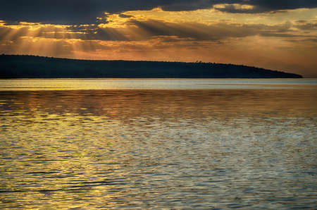 Rays of sun shining through the clouds. The river runs into the distance. The river is calm. The sky is cloudy.の写真素材