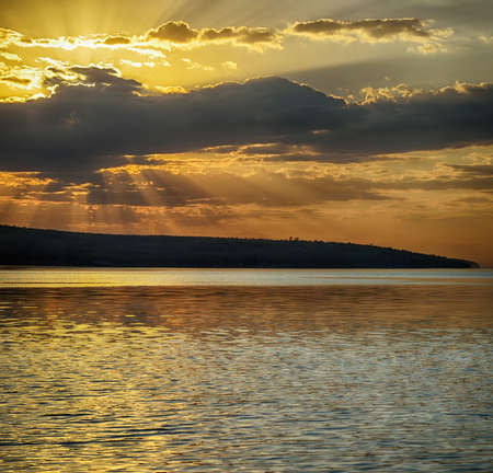 Rays of sun shining through the clouds. The river runs into the distance. The river is calm. The sky is cloudy.の写真素材