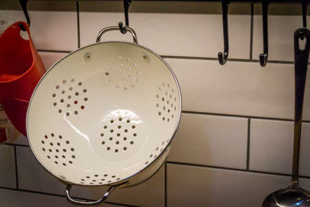 A white metal colander, a kullerder or strainer is hanging on the kitchen wall. Eat.の写真素材