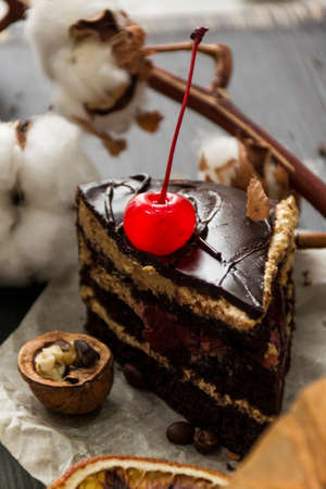 Chocolate cake with a bright cherry. Still life with walnut, coffee grains and a sprig of cotton.の写真素材