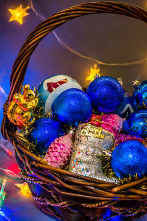 Wicker basket with colored Christmas toys illuminated with festoons.の写真素材