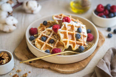 A sweet waffle dessert decorated with berries and nuts in a beautiful sauce-pan on a canvas tablecloth. Natural lightの写真素材