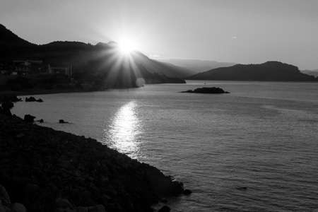 Sunrise from behind the mountains against the backdrop of the sea and the Istavers. Black and white imageの写真素材