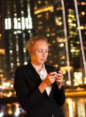 Serious young business woman with the mobile phone in the big city at nightの写真素材