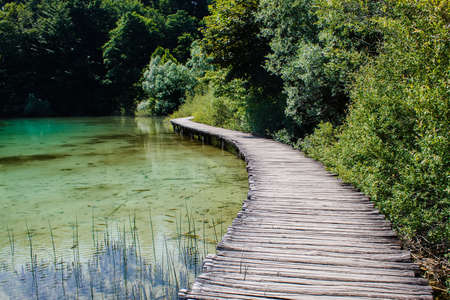 wooden walkway surrounded with crystal clear water and trees in National Pak Plitvice Lakes in Croatiaの写真素材