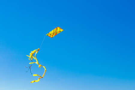 colorful yellow kite with tail in blue skyの写真素材