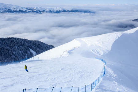 snowboarder on his descent on the trail in mountain ski resort and forest clouds behindの写真素材
