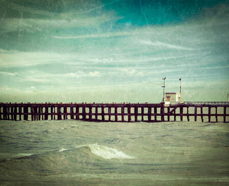 Vintage retro hipster style travel image of  pier in ocean with grunge texture overlaidの写真素材