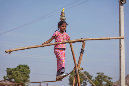 PUSHKAR, INDIA - NOVEMBER 21, 2012: Unidentified indian girl street acrobat walks the tightrope at annual camel fair  Pushkar Mela in Pushkar, Rajasthan, Indiaのeditorial素材