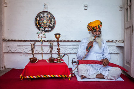 JODHPUR, INDIA - NOVEMBER 26, 2012: Old Indian man smokes hookah (waterpipe) in Mehrangarh fort. The concept of hookah is thought to have originated In Indiaのeditorial素材