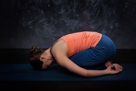 Beautiful sporty fit yogini woman practices yoga asana balasana (child's pose) - resting pose or counter asana for many asanas on dark backgroundの写真素材