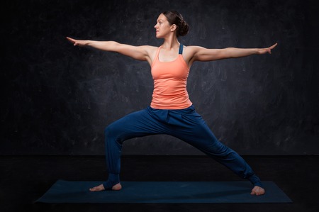 Beautiful sporty fit yogini woman practices yoga asana Virabhadrasana 2 - warrior pose 2 on dark backgroundの写真素材