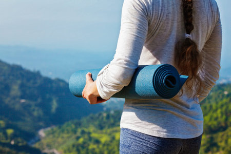 Woman standing with yoga mat outdoors in mountains close up with copyspace getting ready for yoga...
