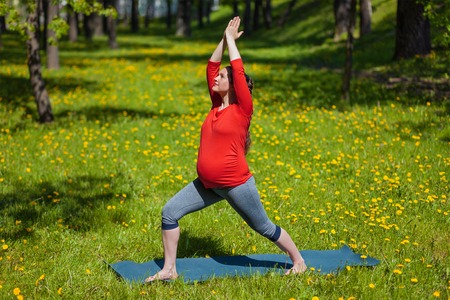 Pregnancy yoga exercise - pregnant woman doing yoga asana Virabhadrasana warrior pose outdoors on grass in summerの写真素材