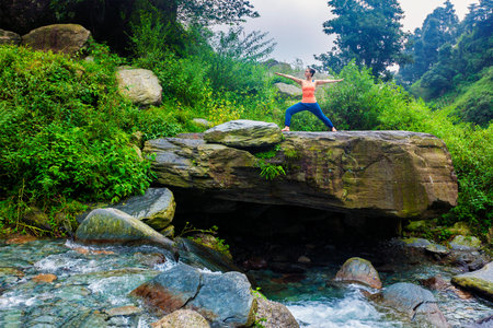 Yoga outdoors - sporty fit woman doing Ashtanga Vinyasa Yoga asana Virabhadrasana 2 Warrior pose...