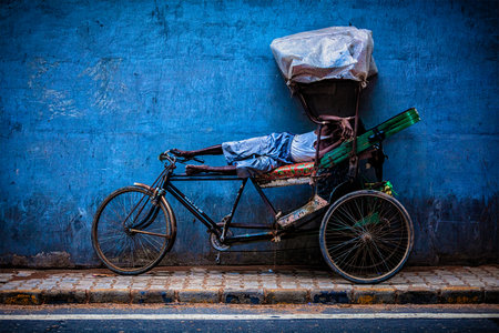 DELHI, INDIA - SEPTEMBER 11, 2011:  Indian cycle rickshaw driver sleeping on his bicycle in the street of New Delhi, India. Cycle rickshaws were used in Kolkata starting about 1930 and are now common in rural and urban areas of India.のeditorial素材