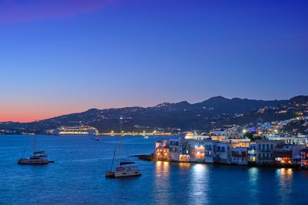 Sunset in Mykonos island, Greece with yachts in the harbor and colorful waterfront houses of Little Venice romantic spot on sunset and cruise ship illuminated in night. Mykonos townd, Greeceの写真素材
