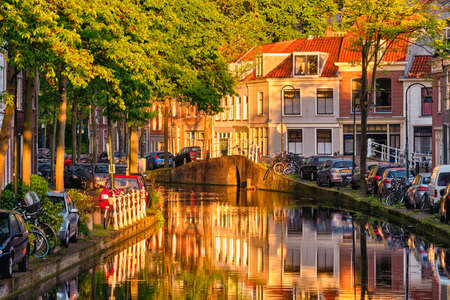 Delt canal with old houses and cars parked along on sunsetの写真素材
