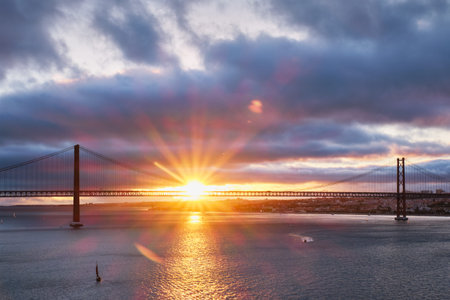 View of 25 de Abril Bridge famous tourist landmark of Lisbon connecting Lisboa and Almada on Setubal Peninsula over Tagus river with tourist yacht boats at sunset. Lisbon, Portugalの写真素材