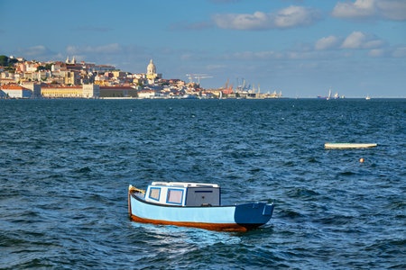 View of Lisbon over Tagus river from Almada with blue fishing boat and yachts tourist boats in...