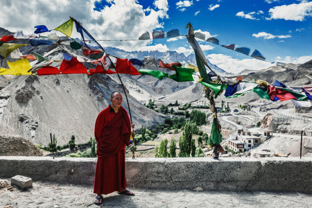 LAMAYURU, INDIA - SEPTEMBER 10, 2011: Buddhist monk standing outside with lugta prayer flags in Lamayuru gompa Buddhist monastery in Ladakh, Indiaのeditorial素材