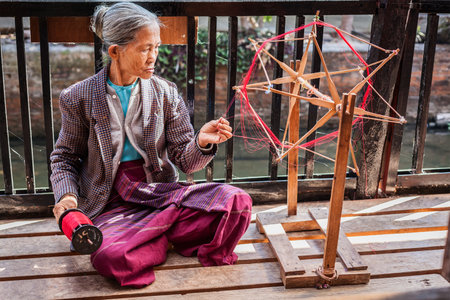 INLE LAKE, MYANMAR - JANUARY 8, 2014: Burmese woman wheel spinning yarn at weaving factory where textile is manufactured in traditional wayのeditorial素材