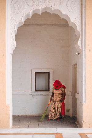 Jodhpur, India - November 13, 2019: Woman in traditional indian Rajasthani clothes sweeping and cleaning the ground with broom in Mehrangarh fort. Jodhpur, Rajasthan, Indiaのeditorial素材