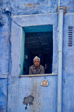 Jodhpur, India - November 13, 2019: Unidentified indian man in window of blue house in Jodhpur, also known as Blue City due to the vivid blue-painted Brahmin houses. Jodhpur, Rajasthan, Indiaのeditorial素材