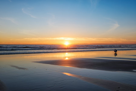 Atlantic ocean sunset with photographer silhouette taking images of surging waves at Fonte da Telha...