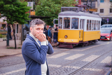 Man in a blue blazer and white sweater standing outdoors in Lisbon city street, Portugal with tram in backgroundの写真素材