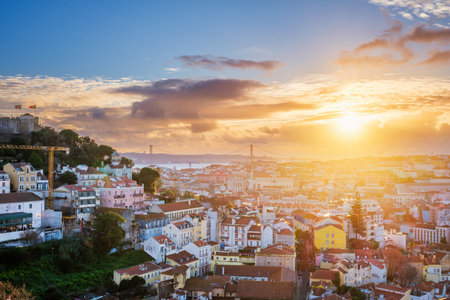 Breathtaking sunset over Lisbon, highlighting the city's rooftops, Carmo Convent ruins, and the iconic 25th of April Bridge. Portugalの写真素材