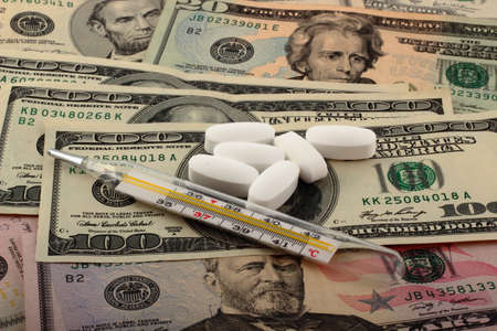 Tablets and thermometer on top of money. The rising cost of health care.の写真素材