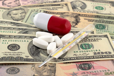 Tablets and thermometer on top of money. The rising cost of health care.の写真素材