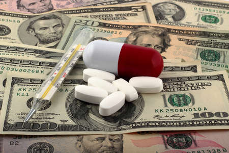 Tablets and thermometer on top of money. The rising cost of health care.の写真素材
