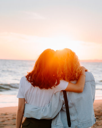 Women hugging on the beach at sunset.の写真素材