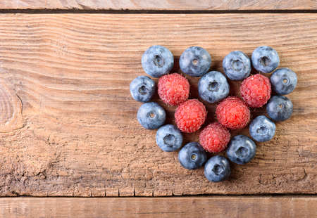 Heart from fresh blueberries and raspberries on an old wooden background top view with copy space. Fresh blueberries. Blueberry. Raspberriesの写真素材